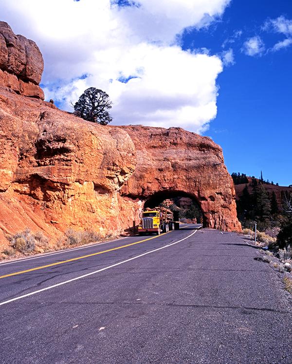 A semi-truck driving through an arch that is made from the mountain on the left of the truck. - TAB Bank